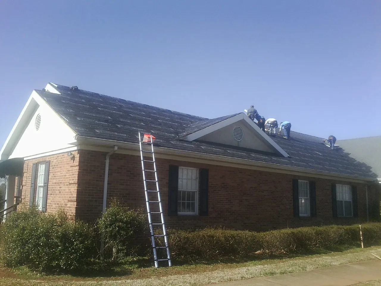 Crew tearing shingles off a brick ranch roof with a ladder set — Metal Roof Repair work by our crew in Thorndale