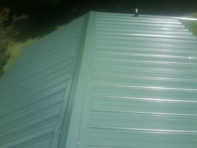 New green metal panels meeting at the ridge of a roof — Flat Roof Repair work by our crew in Thorndale