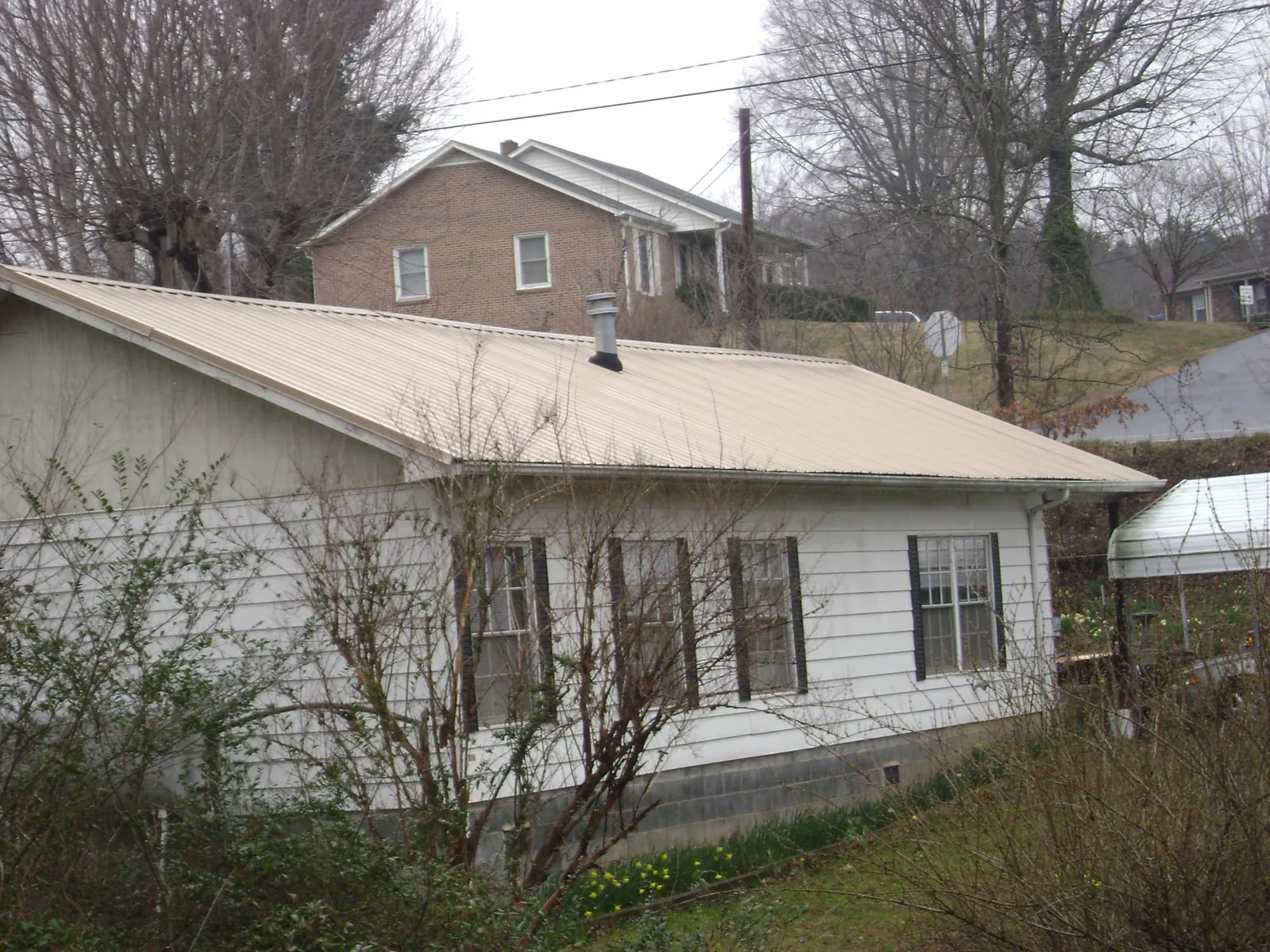 Tan metal roof on a white sided house set into a hillside — Commercial Roofing by Roofing Brothers in Thorndale